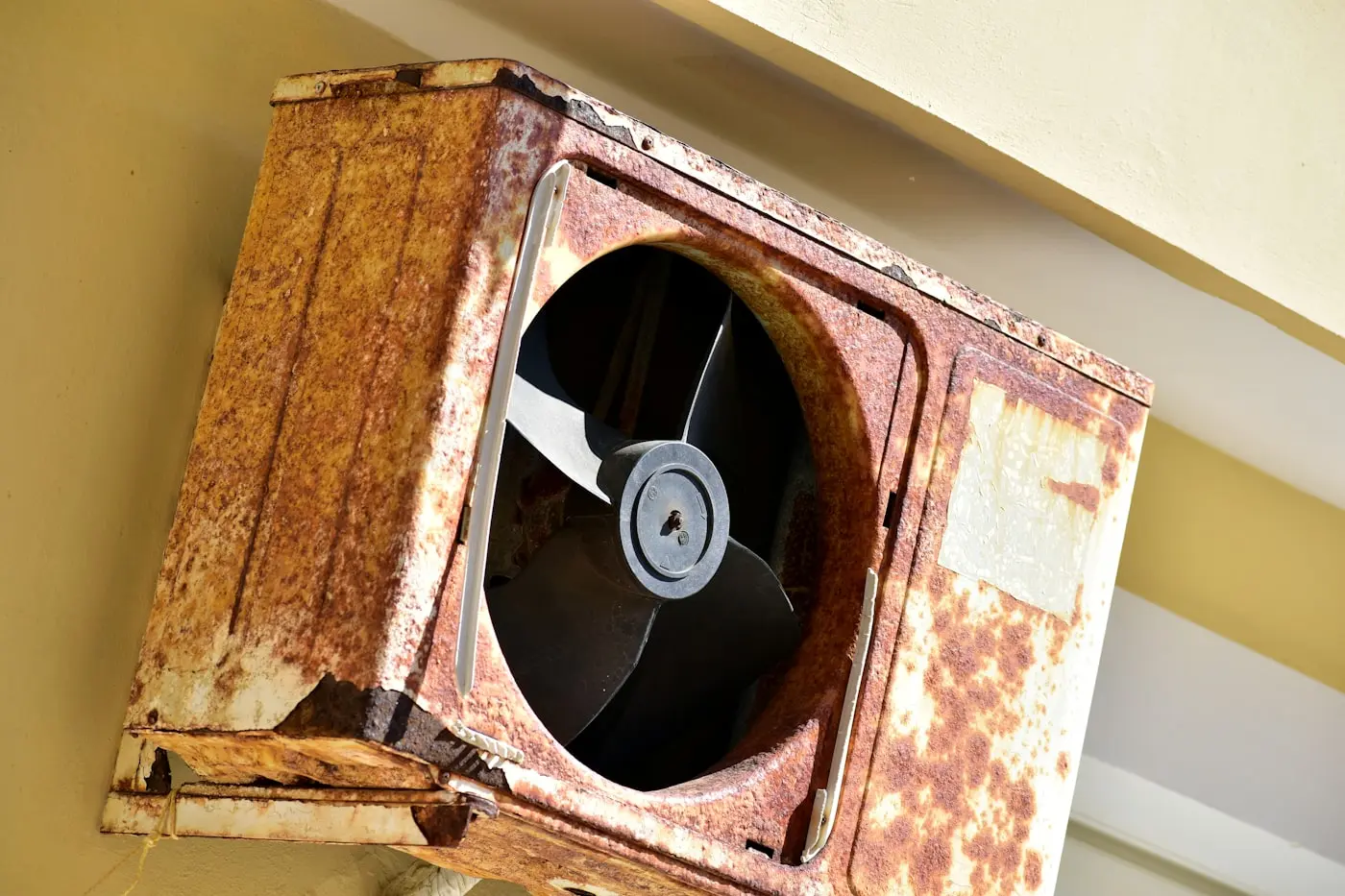 Heavily rusted and grease-caked wall-mounted exhaust fan, overdue for service