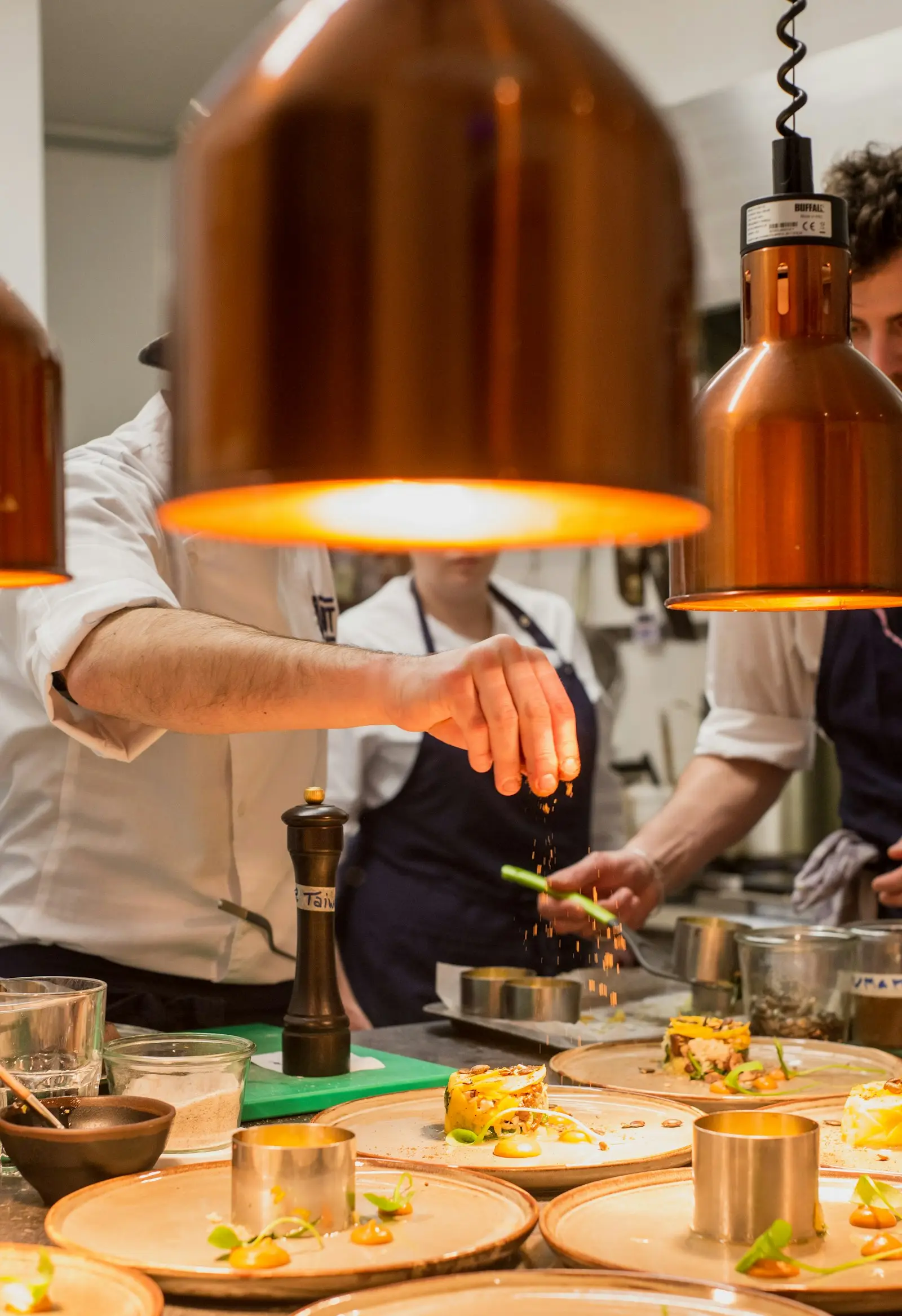 Chefs plating dishes under heat lamps on a busy commercial kitchen pass