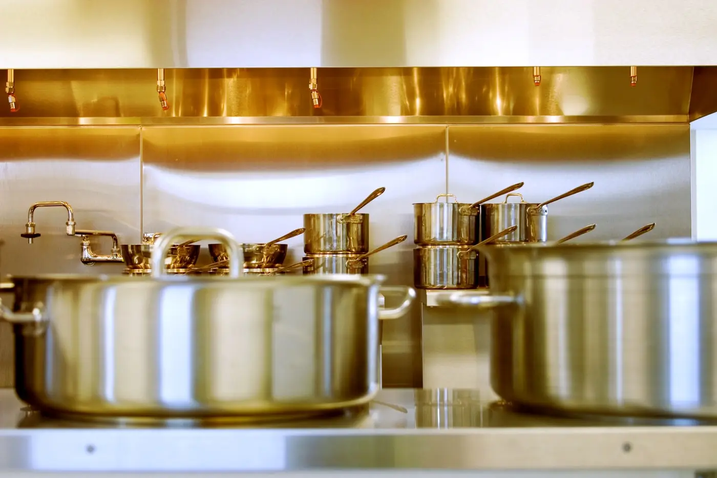 Stainless commercial canopy above a clean cooking line with polished pans beneath