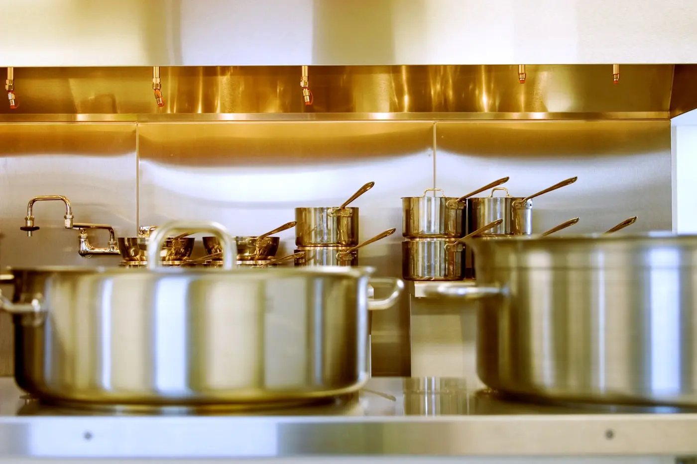 Stainless commercial canopy above a clean cooking line with polished pans beneath